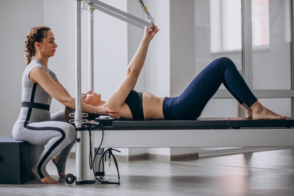 Porque es mejor Pilates con máquinas. Instructor corrigiendo la postura de un alumno en pilates con máquina.